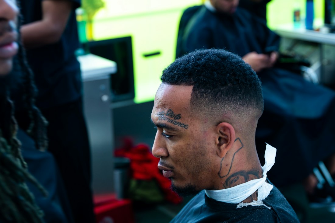 Man in a barber chair with a low taper fade and short curly top, seen in profile
