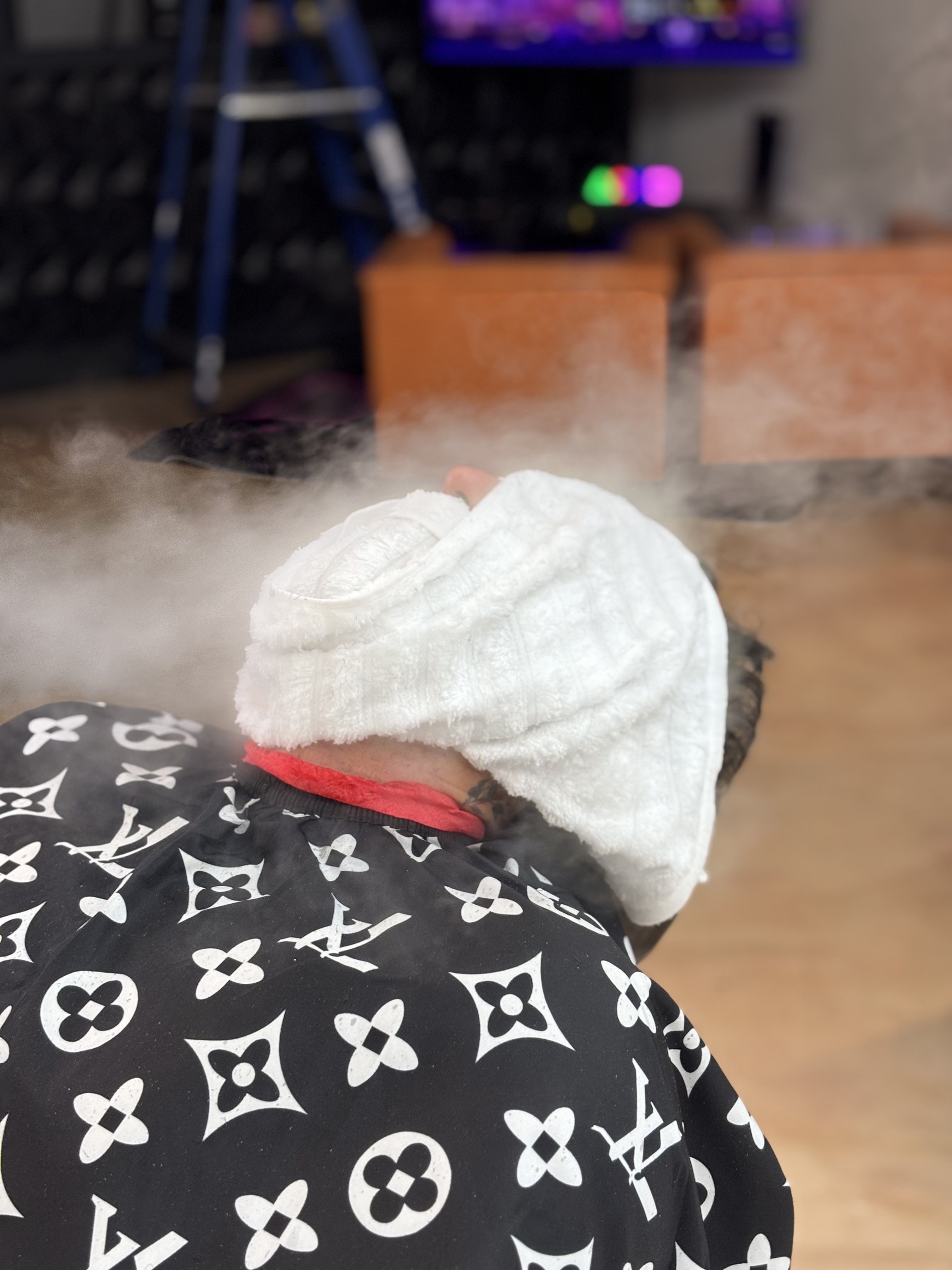 Client reclined in the barber chair with a hot towel over his face at God Level Barbershop